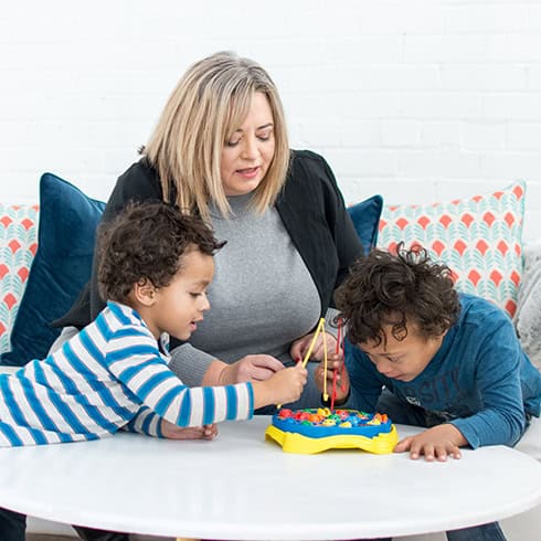 Woman and two children playing a colorful board game together, promoting communication and social sk.