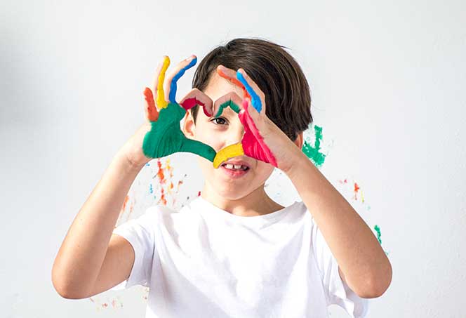 Child playing with colorful paint-covered hands, demonstrating creativity and communication skills.
