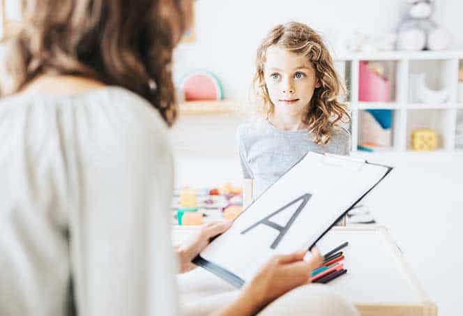 Child learning communication skills with a speech therapist in a bright, welcoming therapy room.