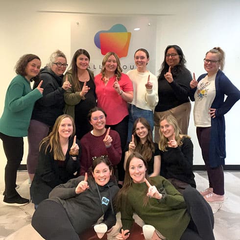 Group of diverse women smiling and holding up one finger during a communication training session.
